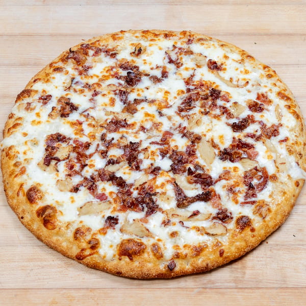 Round pizza with white sauce, melted cheese, bacon, and chicken on a wooden surface.