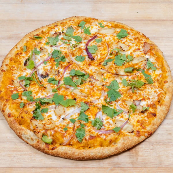 A whole pizza with chicken, red onions, and cilantro on a wooden surface.