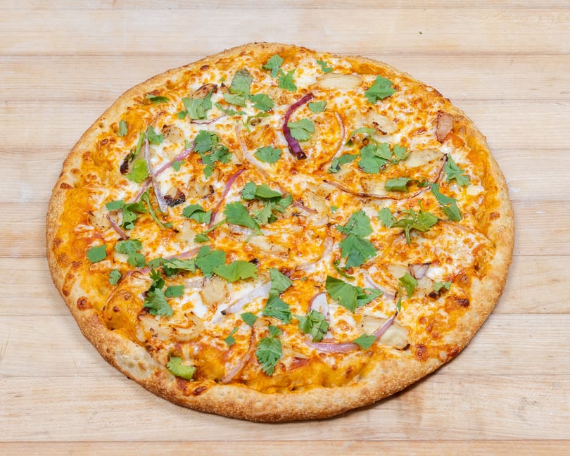 A whole pizza with chicken, red onions, and cilantro on a wooden surface.