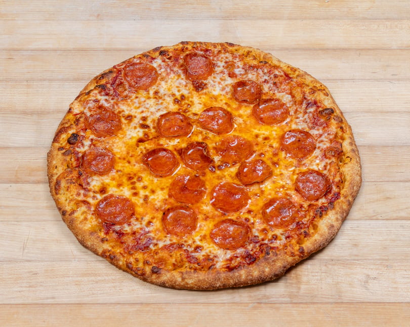 A whole pepperoni pizza with melted cheese and a golden crust, centered on a light wooden surface.
