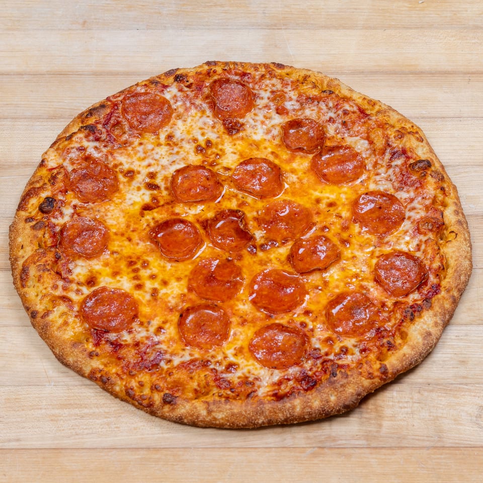 A whole pepperoni pizza with melted cheese and a golden crust on a light wooden surface.