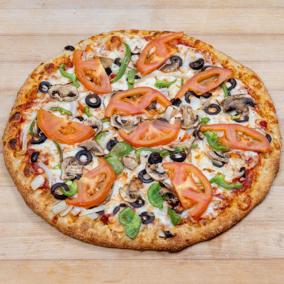 A whole vegetarian pizza with tomatoes, mushrooms, olives, onions, and green peppers on a wooden surface.