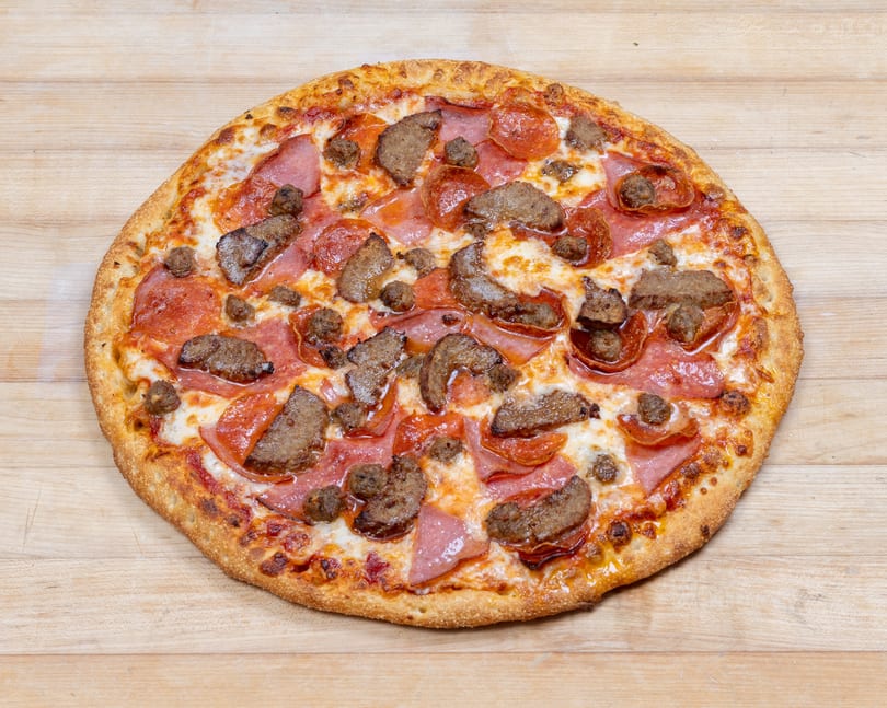 A whole meat lover's pizza with pepperoni, ham, and sausage on a wooden surface.