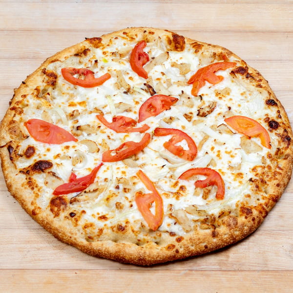 A whole pizza with white sauce, chicken, onions, and tomato slices on a wooden surface.