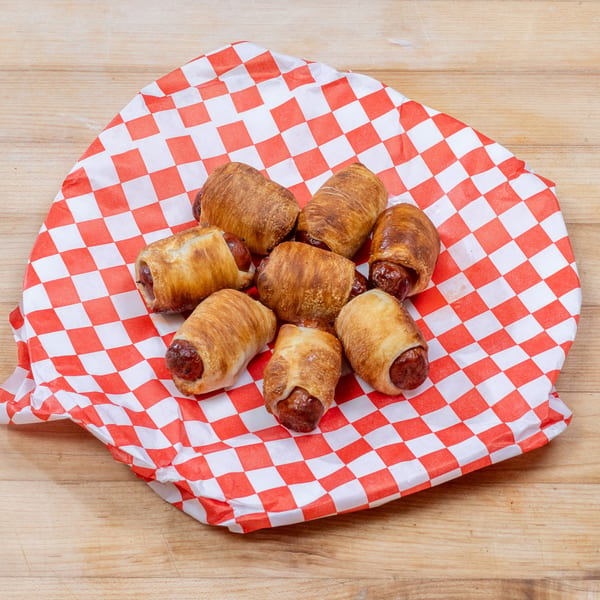 Seven pigs in a blanket, wrapped in golden pastry, on red and white checkered paper.
