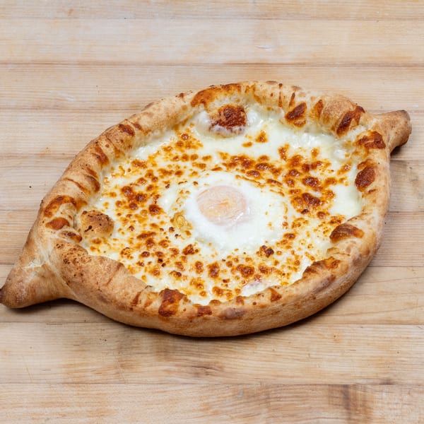 Adjaruli Khachapuri, a Georgian cheese bread boat with a baked egg in the center, on a wooden surface.