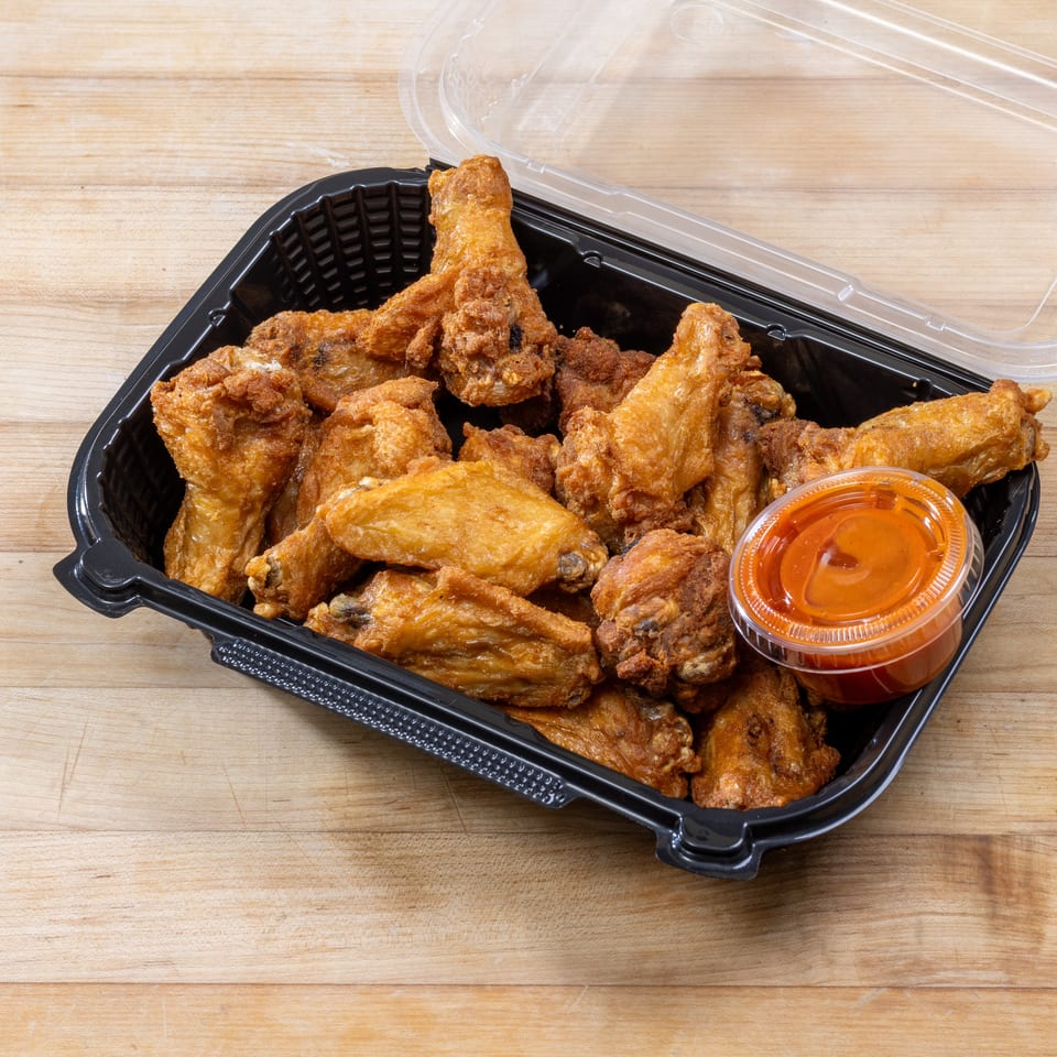Crispy fried chicken wings and a small container of hot sauce in a black to-go box.