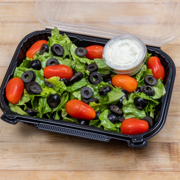 Fresh green salad with cherry tomatoes, black olives, and ranch dressing in a to-go container.